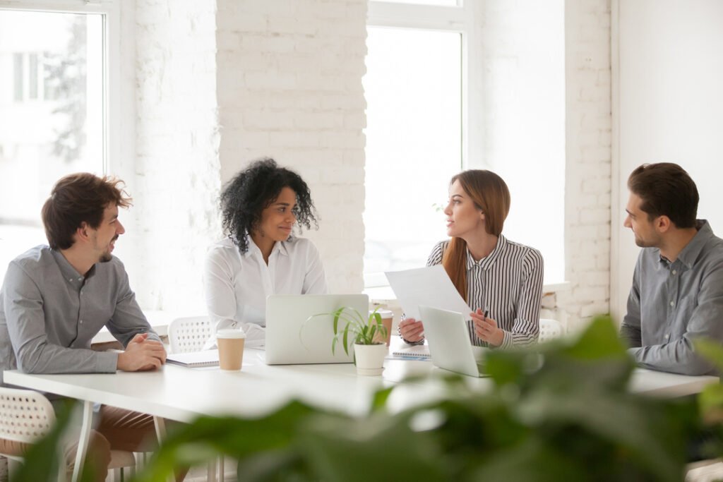 Comunicação colaborativa: colegas de trabalho compartilham ideias sentados ao redor de uma mesa em uma sala.