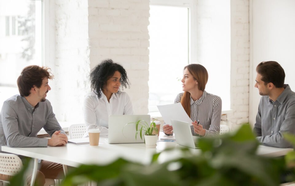 Comunicação colaborativa: colegas de trabalho compartilham ideias sentados ao redor de uma mesa em uma sala.