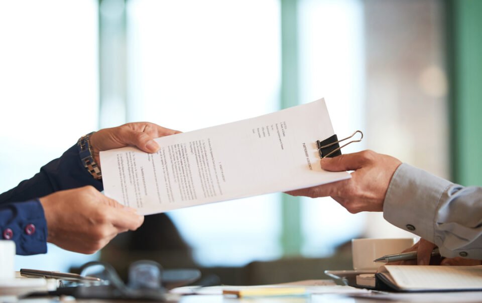 Profissionais em um escritório passando um documento entre si que representa o pedido de venda.