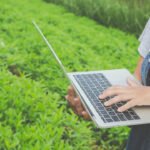Foto mostra profissional com laptop em meio a uma plantação, mostrando a transformação da tecnologia e necessidade do ERP para agronegócio.